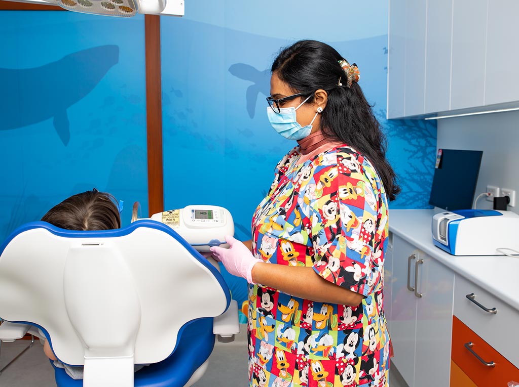 NLPD dental team member preparing equipment beside a young patient in the treatment chair