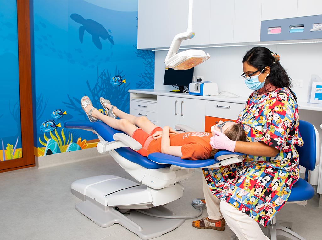 Specialist paediatric dentist examining a young patient in a treatment room with an ocean mural